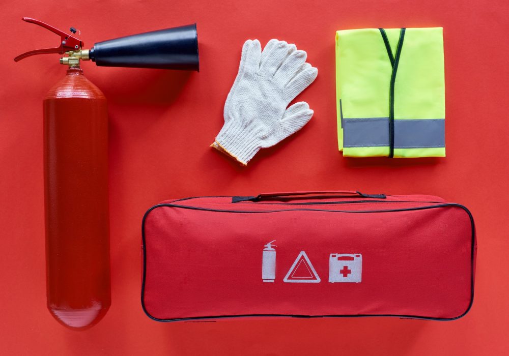 top view of automotive handbag, reflective vest, gloves and fire extinguisher on red background